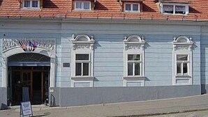 A building with a red-tiled roof, a white facade, and a small entrance with a decorative archway. - Várkapu Panzió (Eger)