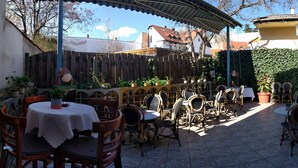 An outdoor patio with tables and chairs, surrounded by a wooden fence and potted plants. - Várkapu Panzió (Eger)
