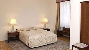A bedroom with a bed, two bedside lamps, a wooden floor, a chandelier, a window with curtains, and a wooden wardrobe. - Várkapu Panzió (Eger)