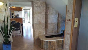 A lobby with a stone wall, a reception desk, and a potted plant. - Hotel Marom (Haifa)