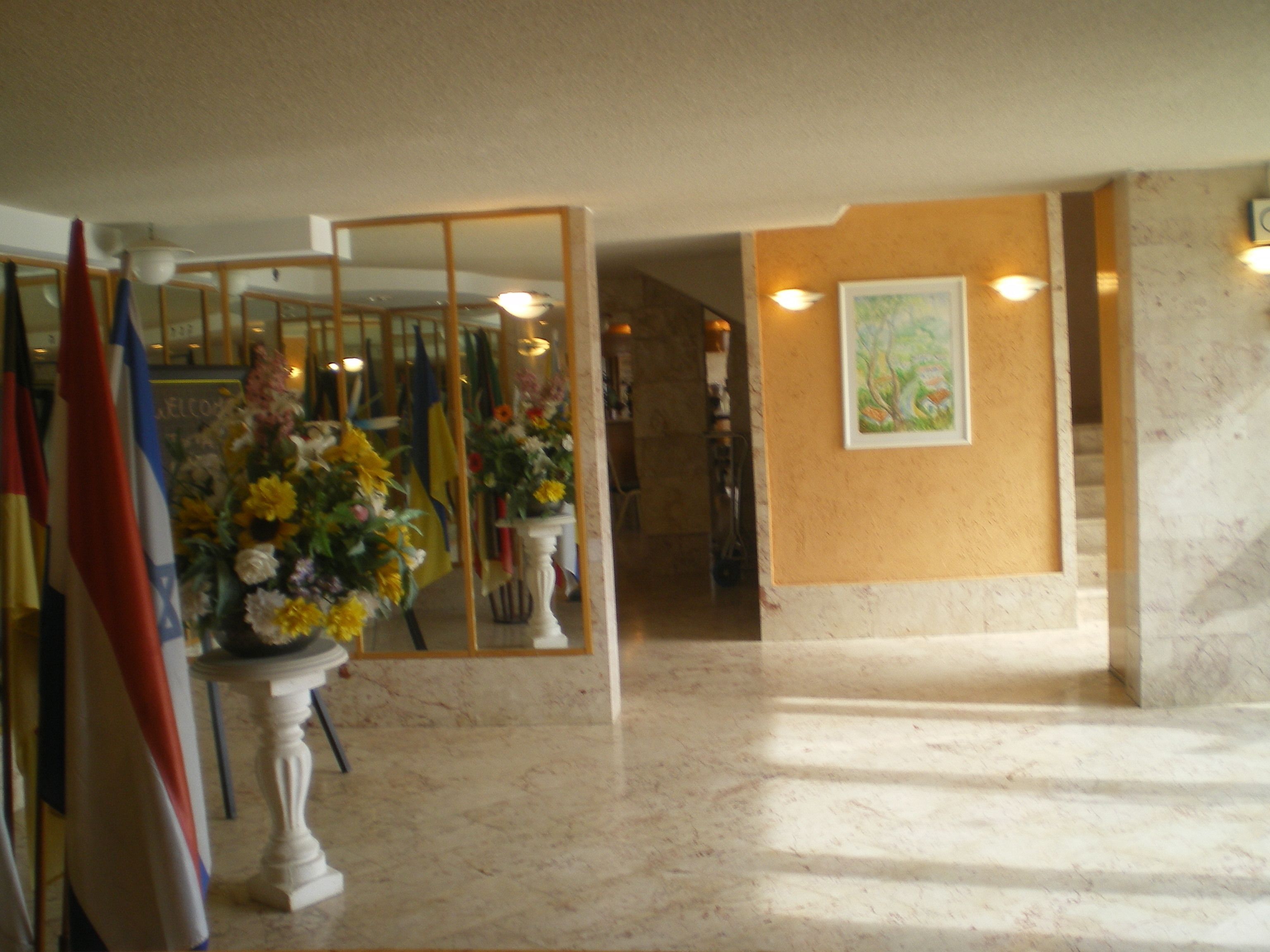 A marble-floored hallway with a large mirror reflecting the room, a staircase, and a painting on the wall.