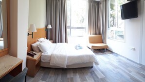 A hotel room with a bed, a chair, a desk, a lamp, and a TV. - Hotel Marom (Haifa)