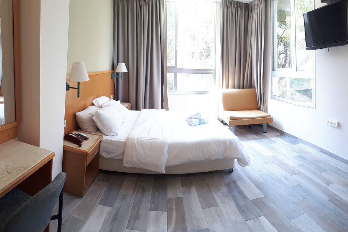 A hotel room with a bed, a chair, a desk, a lamp, and a TV.