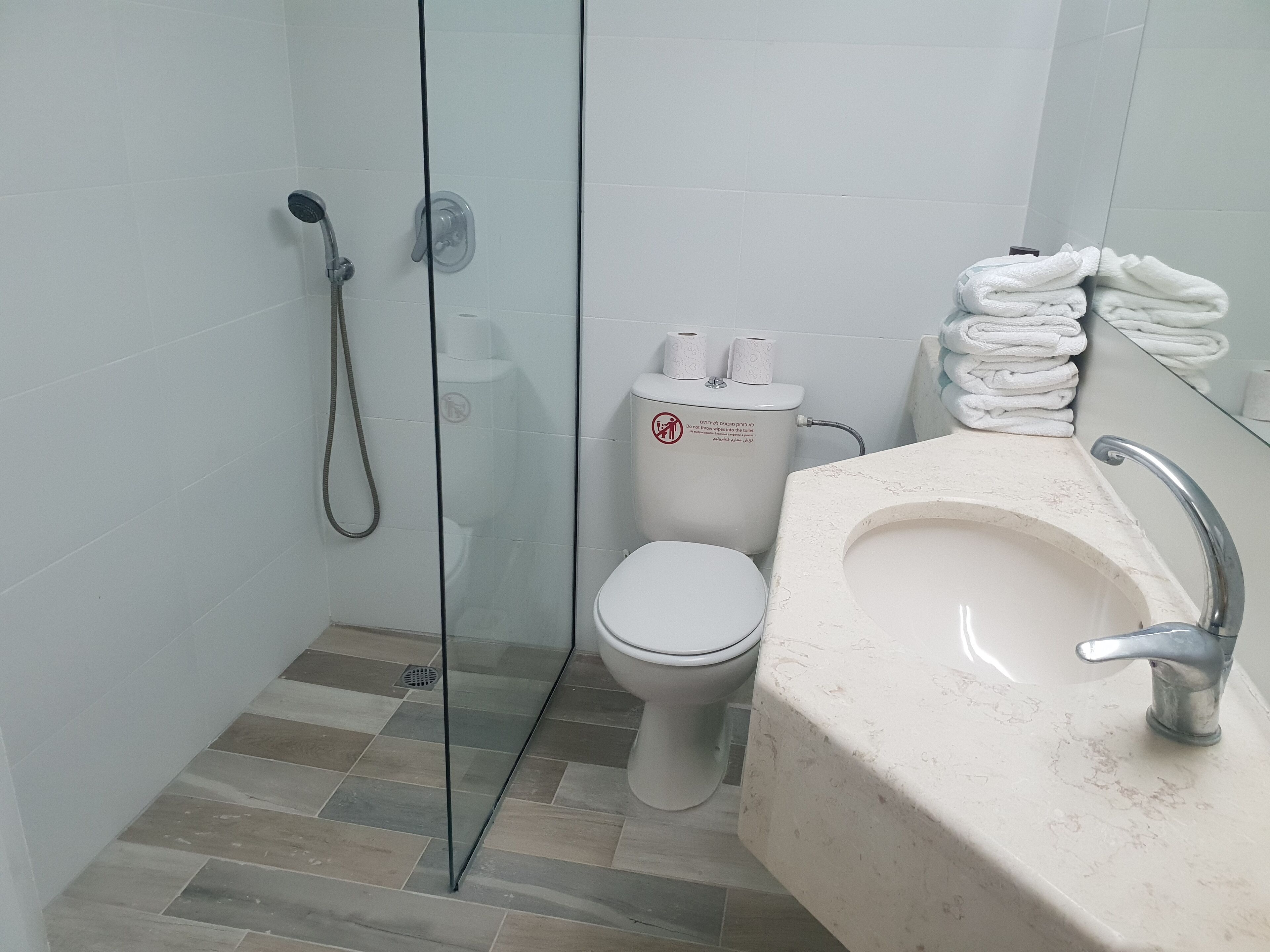 Een badkamer met een douchecabine van glas, een toilet en een wastafel met spiegel.