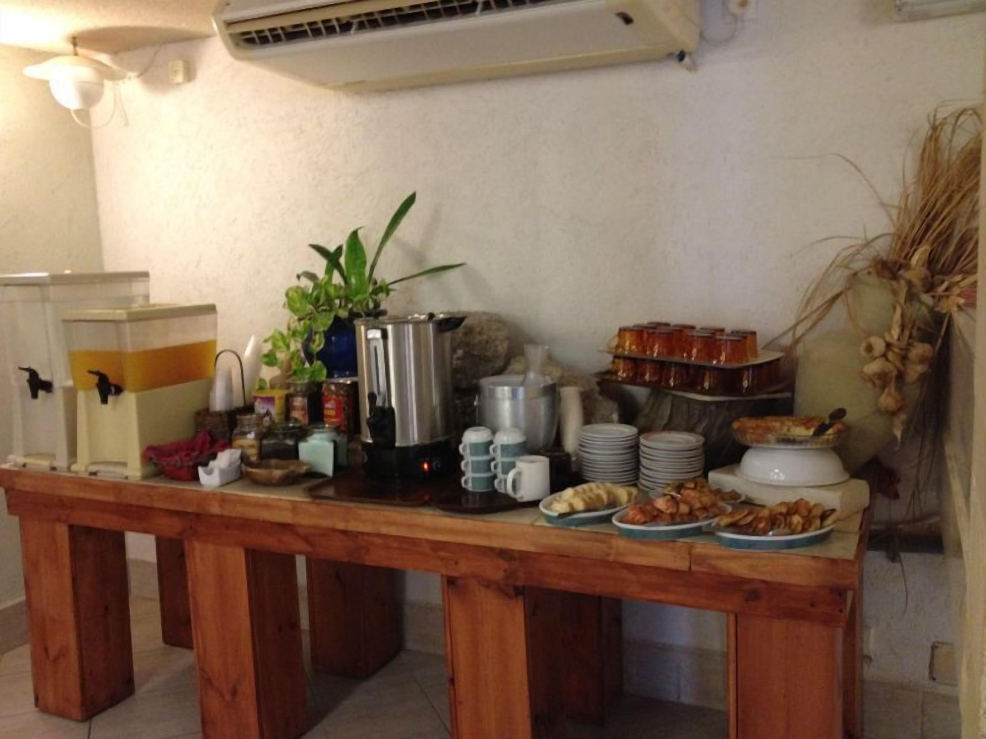 Una mesa de madera con un bufé de desayuno que incluye una cafetera, platos y diversos alimentos.