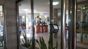 A modern lobby with glass doors, a reception desk, and a dining area with a wooden table and chairs. - Hotel Marom (Haifa)