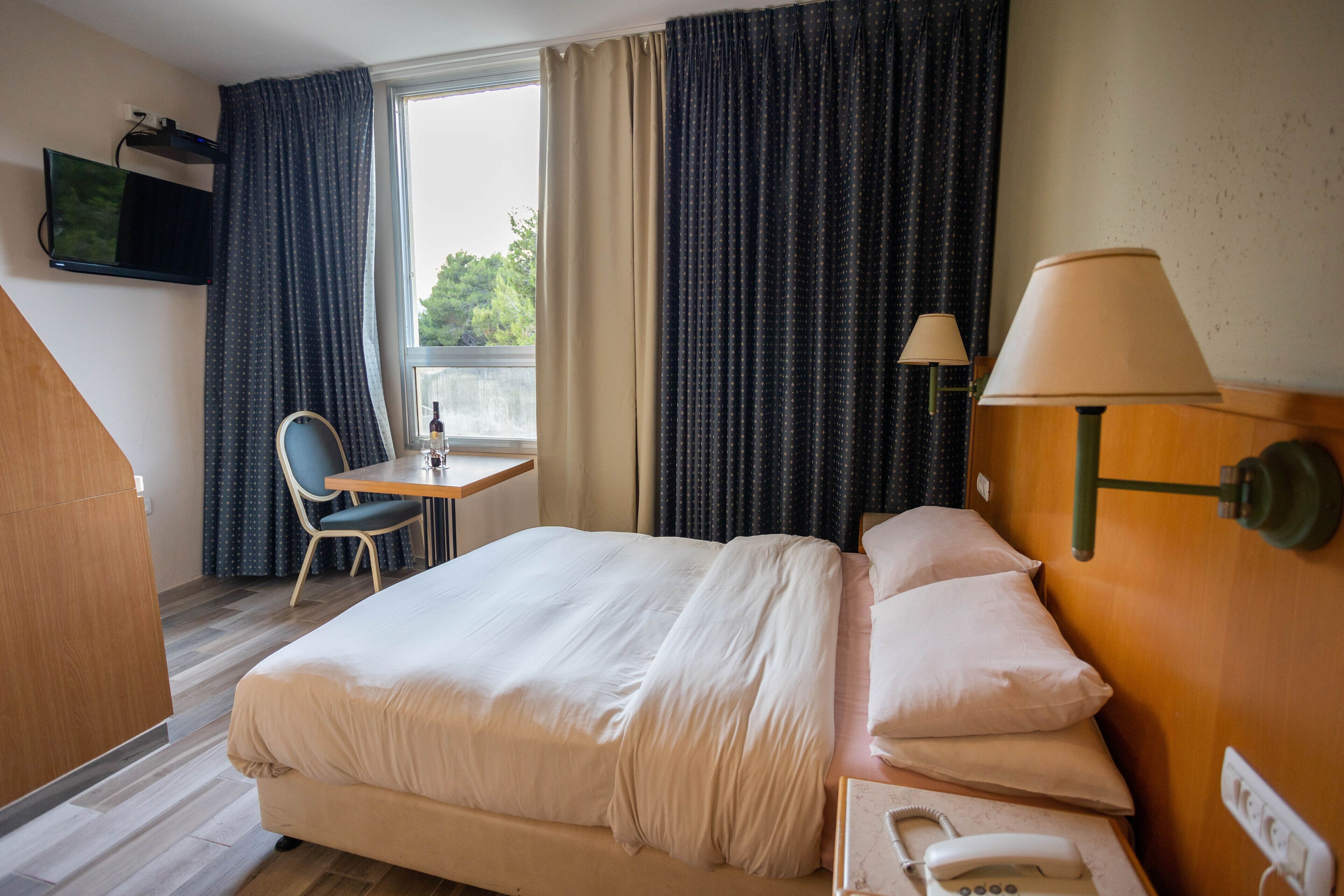 A hotel room with a bed, a desk, a chair, a TV, and a lamp.