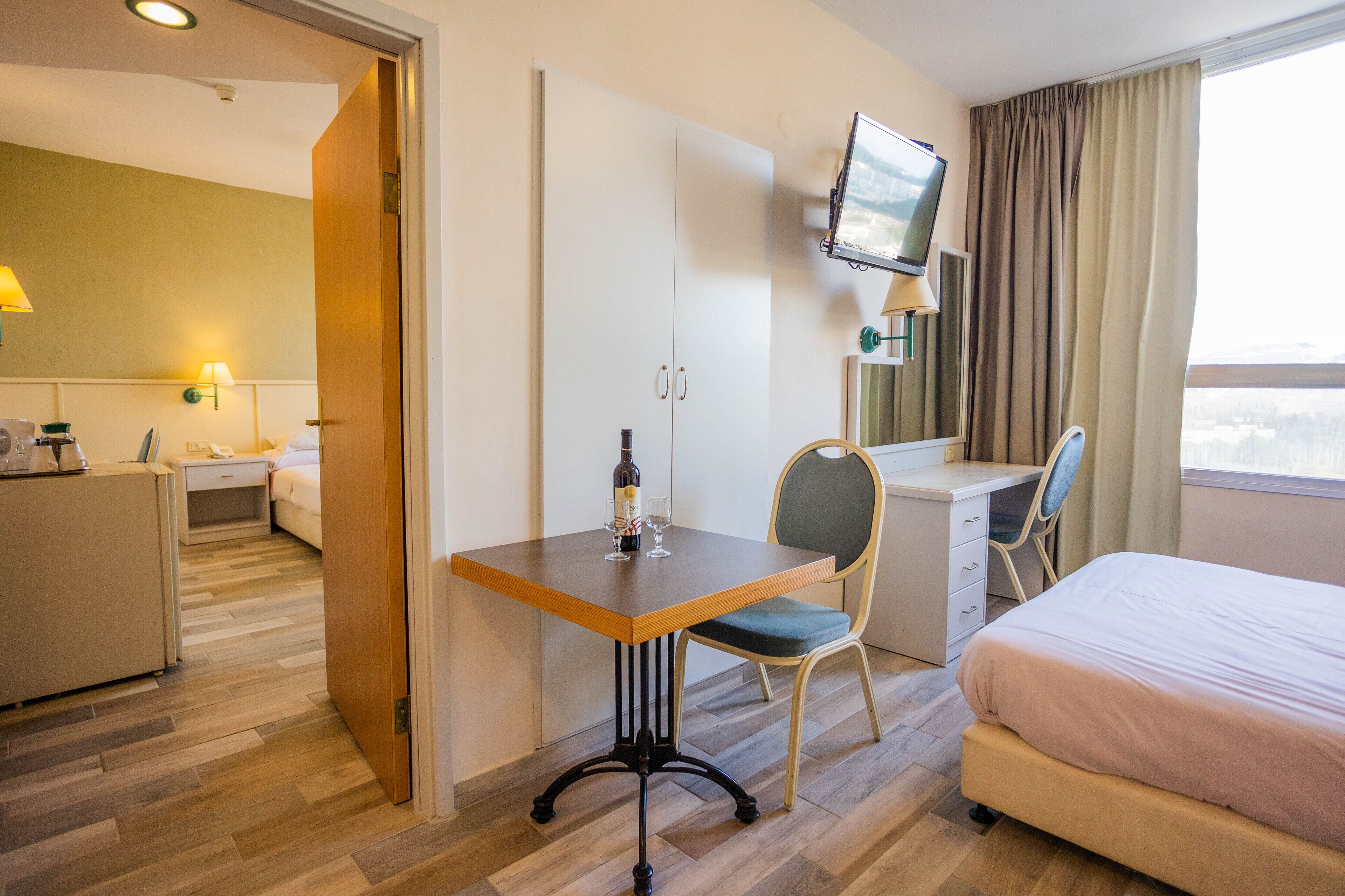 A hotel room with a bed, a desk with a chair, a television mounted on the wall, and a window with curtains.