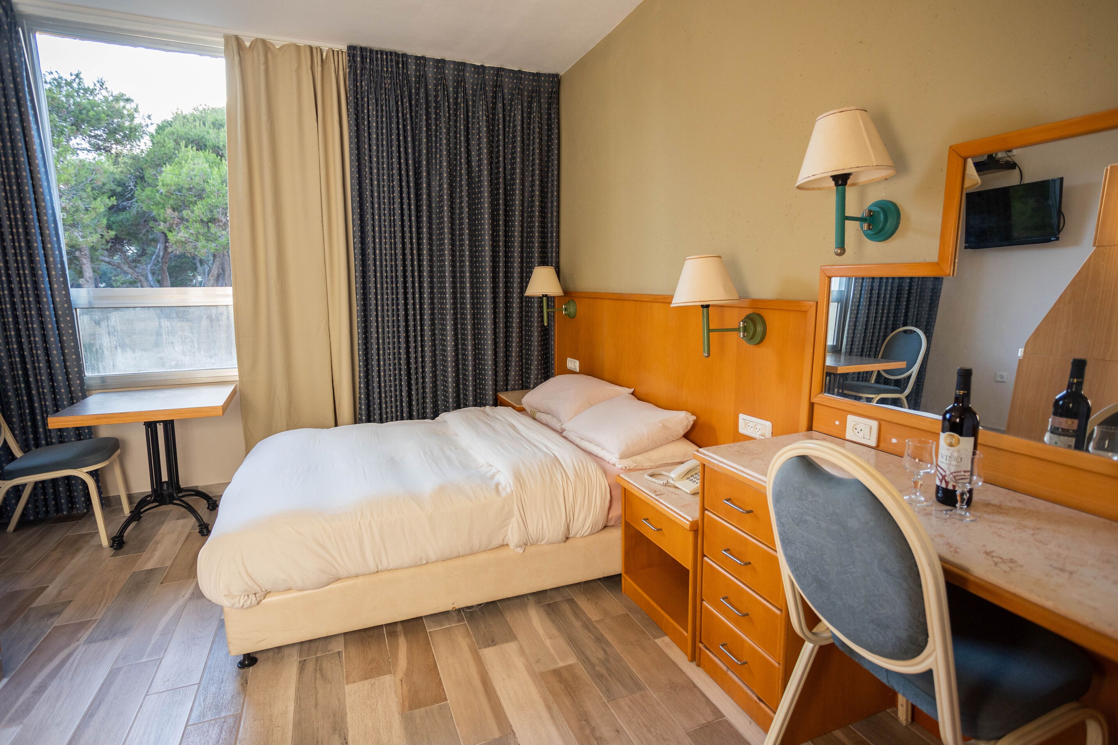 A hotel room with a bed, desk, chair, and a window with curtains.