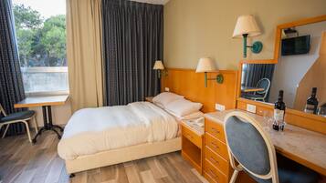 A hotel room with a bed, desk, chair, and a window with curtains.