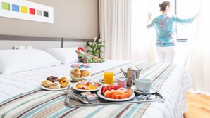 Una cama bien tendida con una bandeja de desayuno, una ventana con cortinas y una pared con muestras de color.