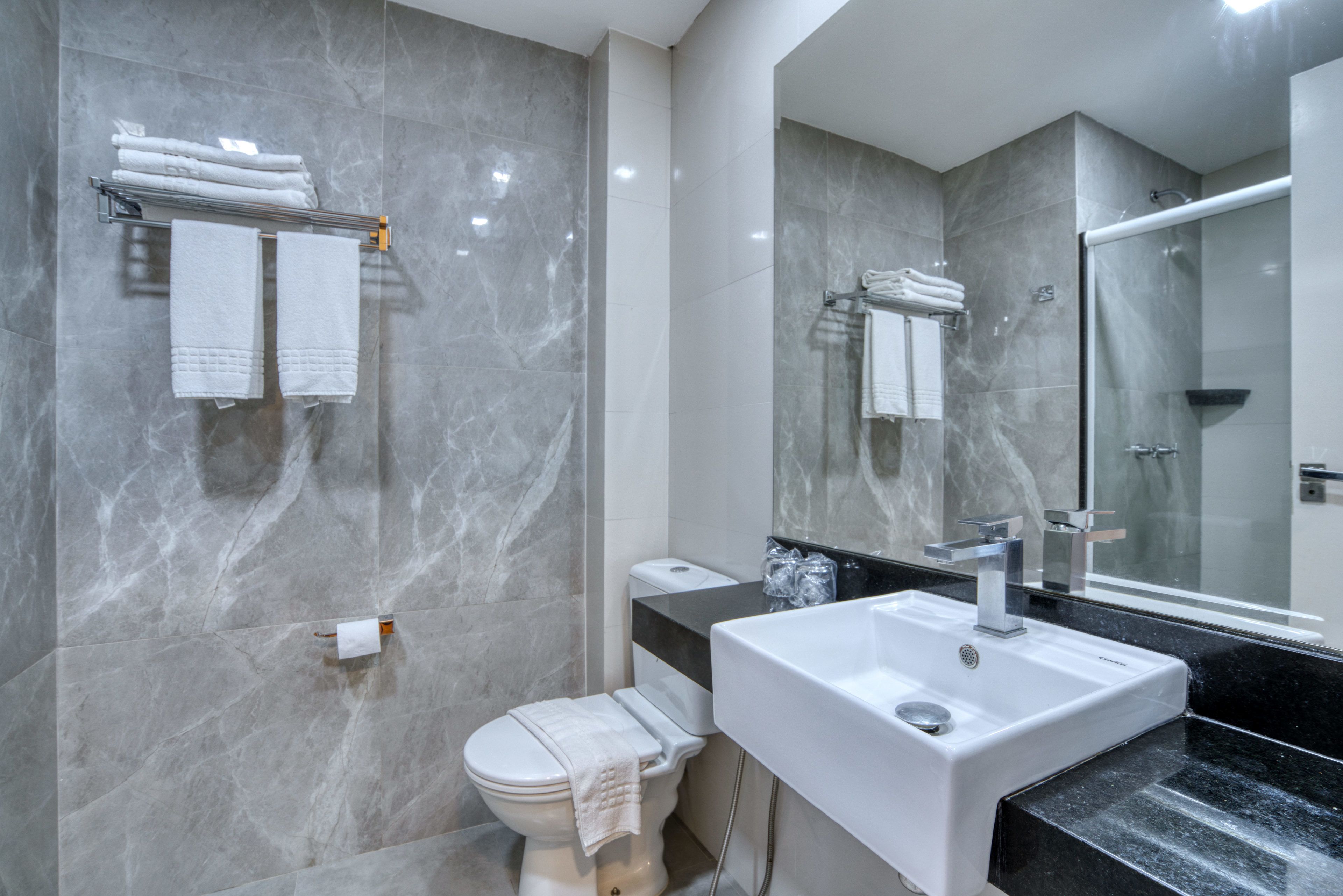 A modern bathroom with a marble wall, a white toilet, a sink with a mirror, and a glass shower enclosure.