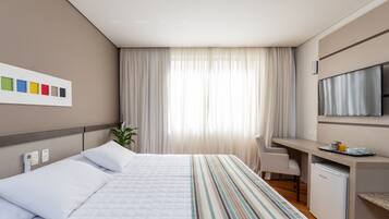 A hotel room with a bed, a desk, a television, and a plant.