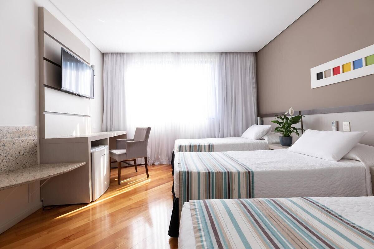 A hotel room with a bed, a desk, a chair, and a TV.