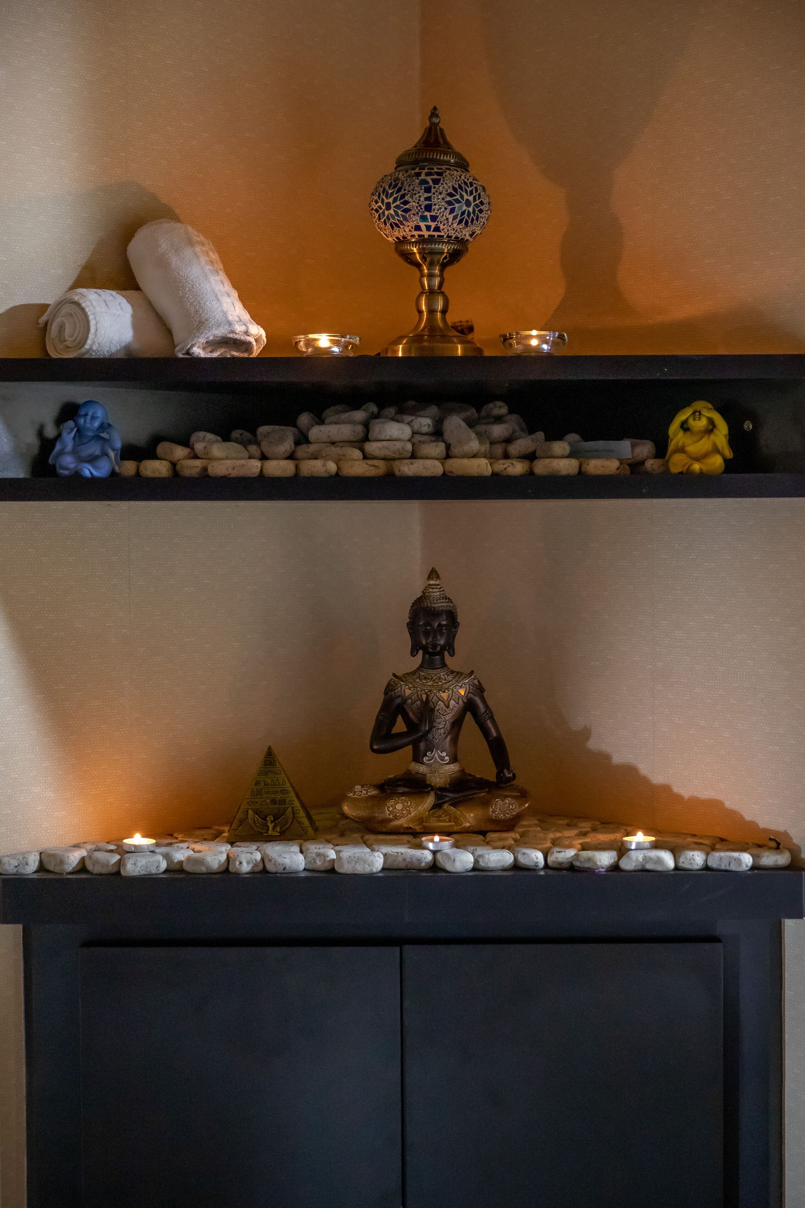 A shelf with a Buddha statue, a decorative lamp, and a small Buddha figurine.
