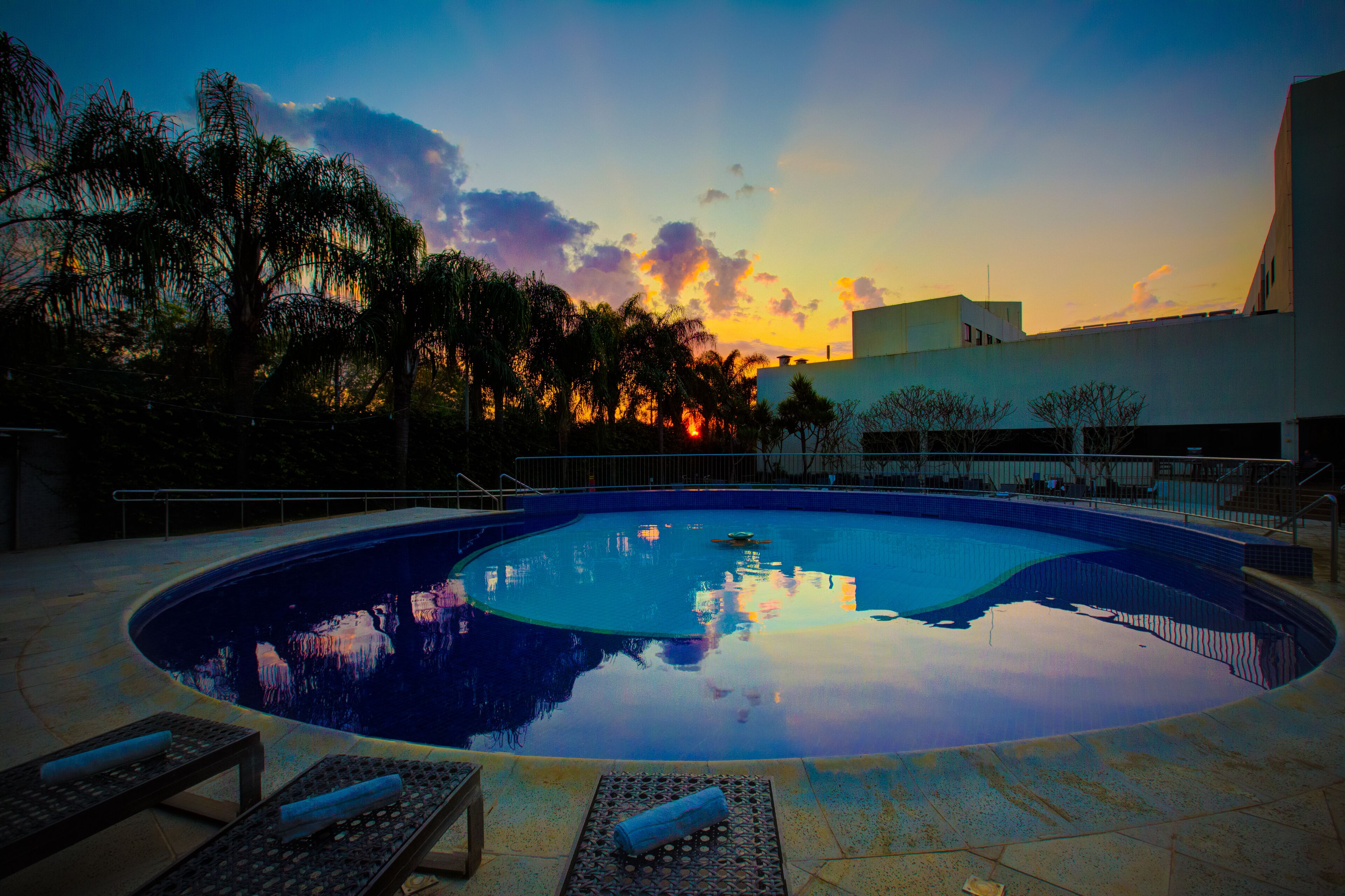 A swimming pool with lounge chairs and a sunset view.