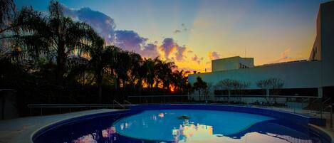 A swimming pool with lounge chairs and a sunset view.