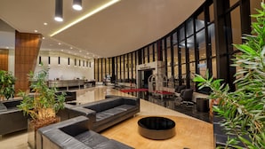 Un moderno vestíbulo de hotel con una zona de estar curvada, un mostrador de recepción y grandes ventanales.