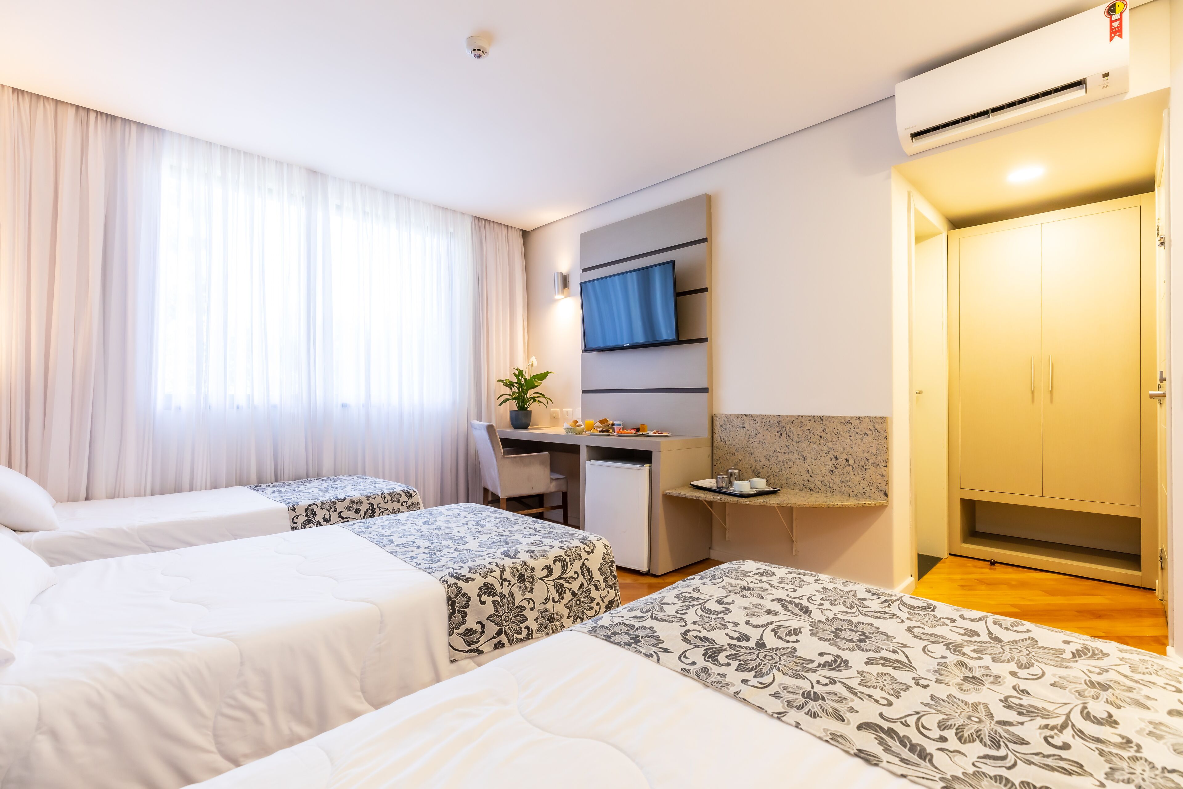 Ein Hotelzimmer mit zwei Betten, einem Schreibtisch, einem Fernseher und einem Kleiderschrank.