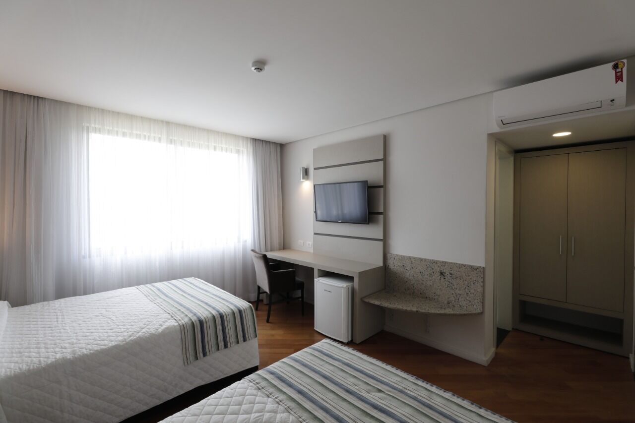 Ein Hotelzimmer mit zwei Betten, einem Schreibtisch, einem Fernseher und einem Kleiderschrank.