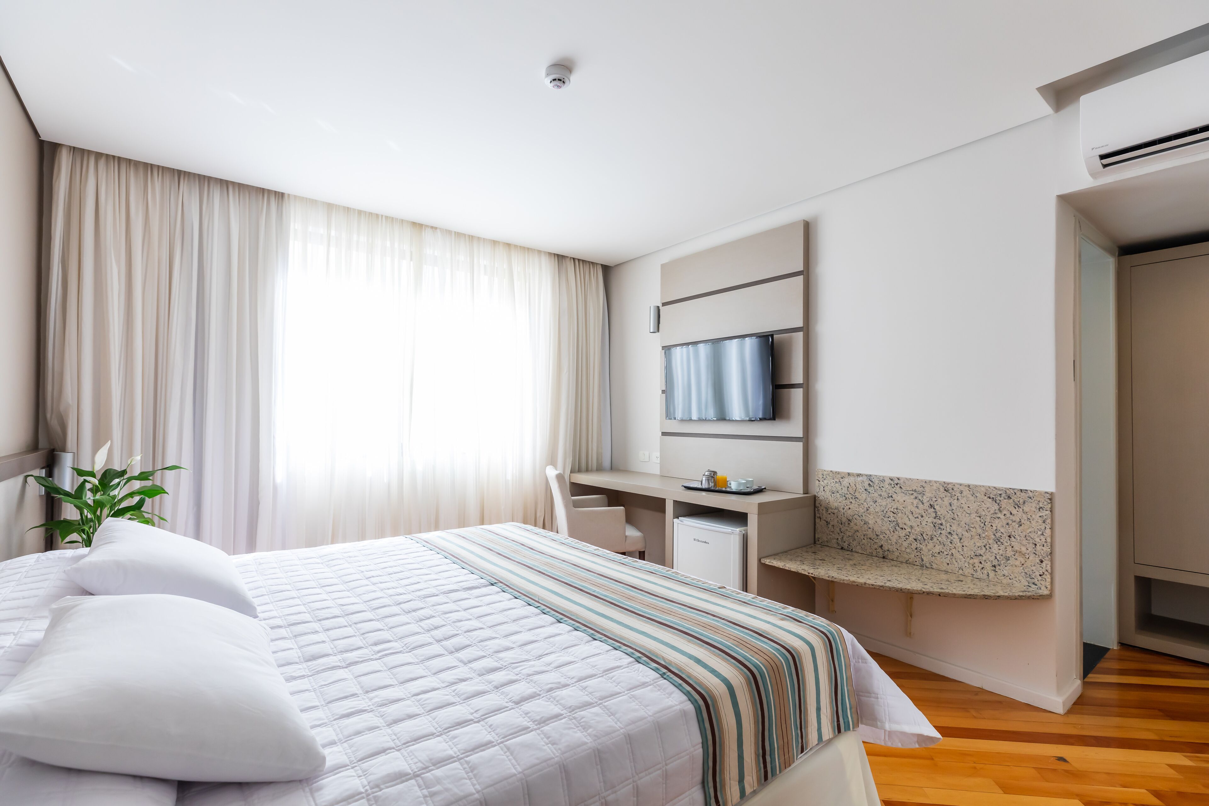 Habitación de hotel con cama, escritorio, televisión y un pequeño rincón de descanso.