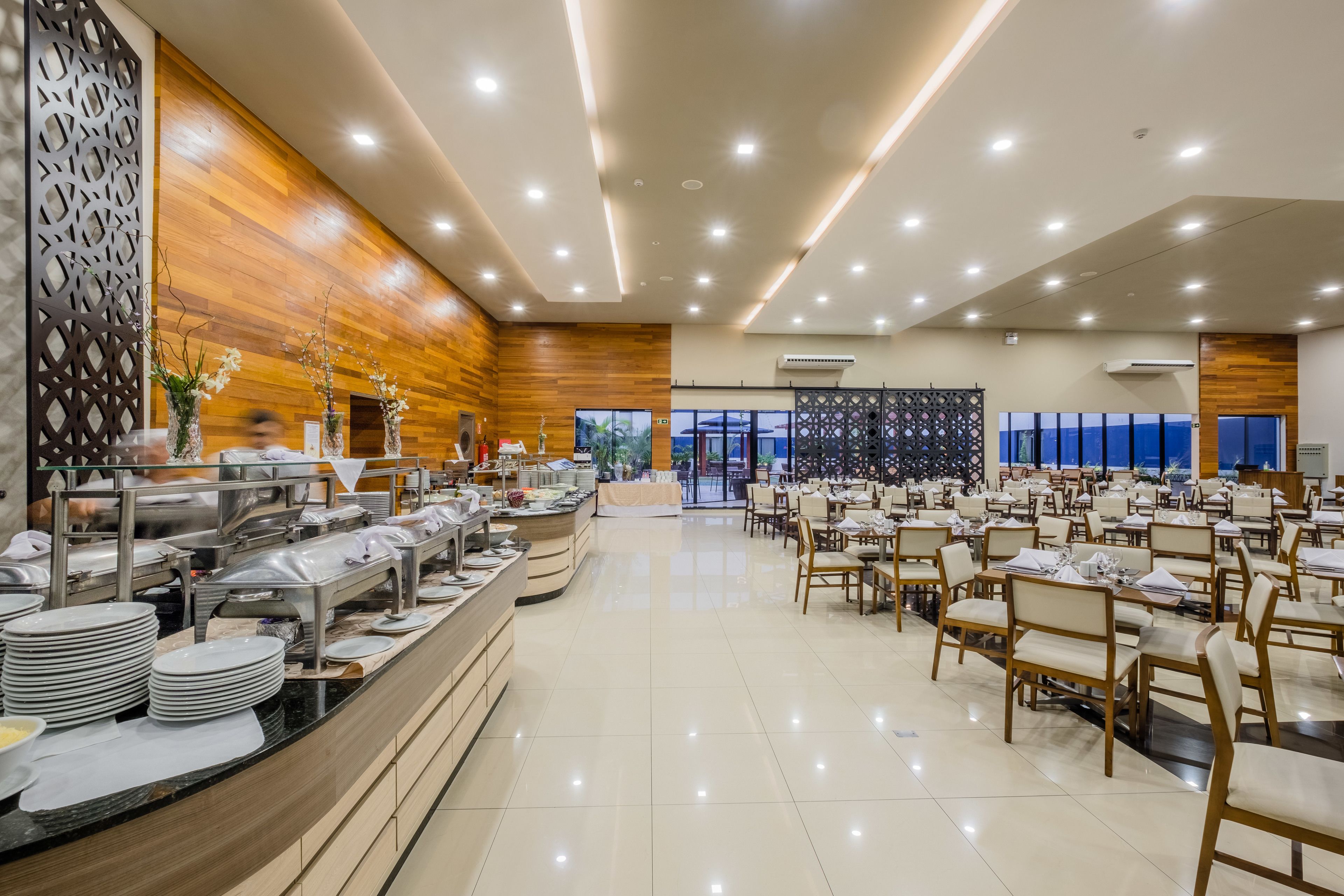 A spacious dining area with multiple tables and chairs, a buffet counter with various food items, and a wooden wall with a decorative panel.