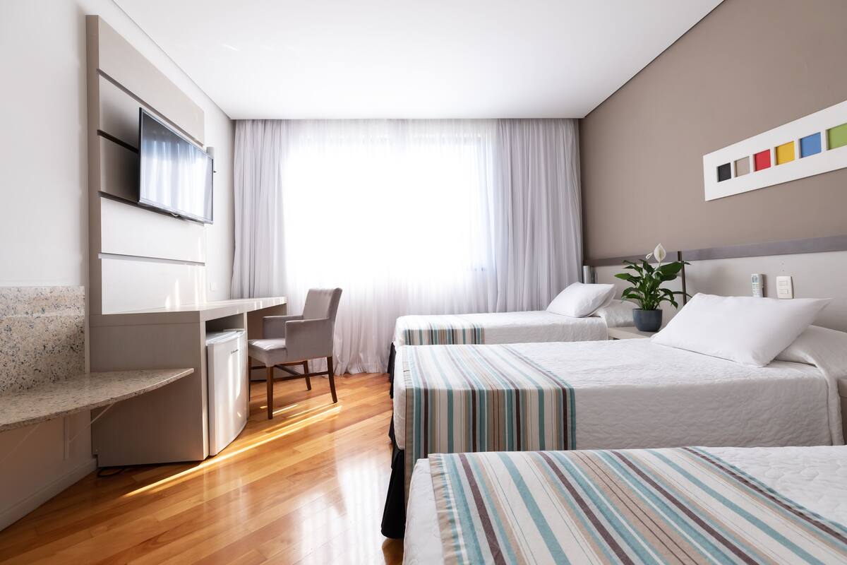 A hotel room with two beds, a desk, a chair, a TV, and a window with curtains.
