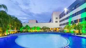 A swimming pool with a curved edge, surrounded by a building with multiple floors and balconies.