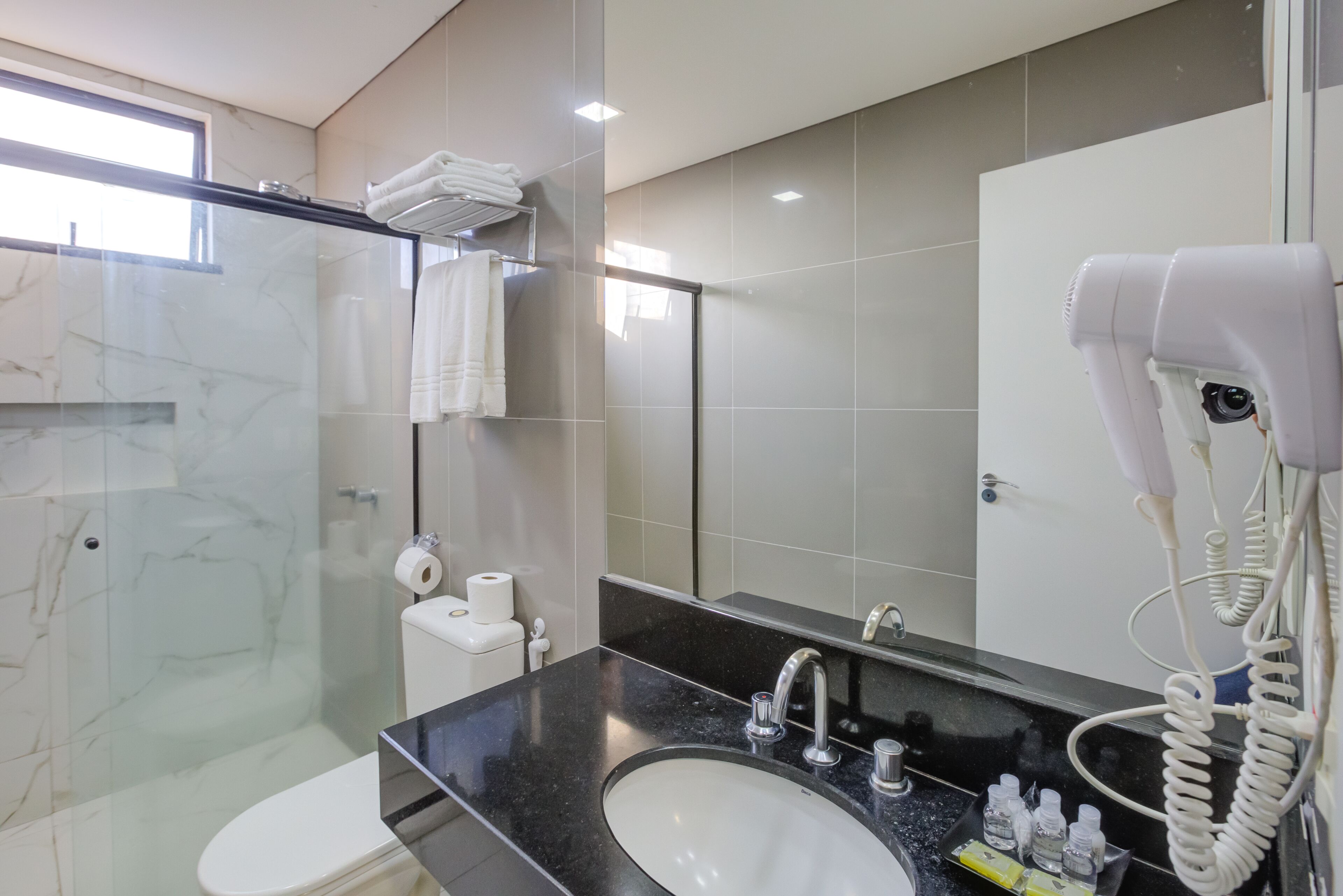 Une salle de bain moderne dotée d’une douche à parois de verre, d’un lavabo à poser de couleur noire et d’un sèche-cheveux fixé au mur.