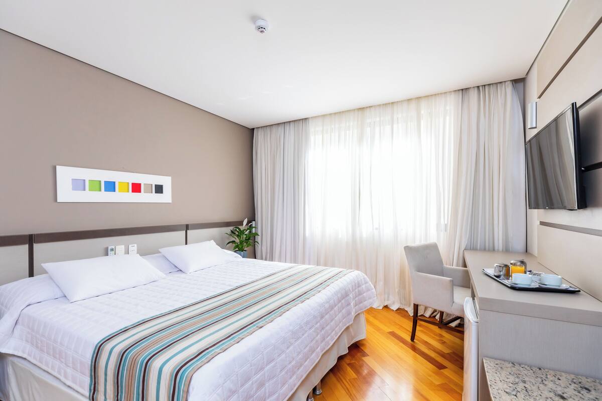 A modern hotel room with a large bed, a desk with a tray of breakfast items, and a mounted TV.