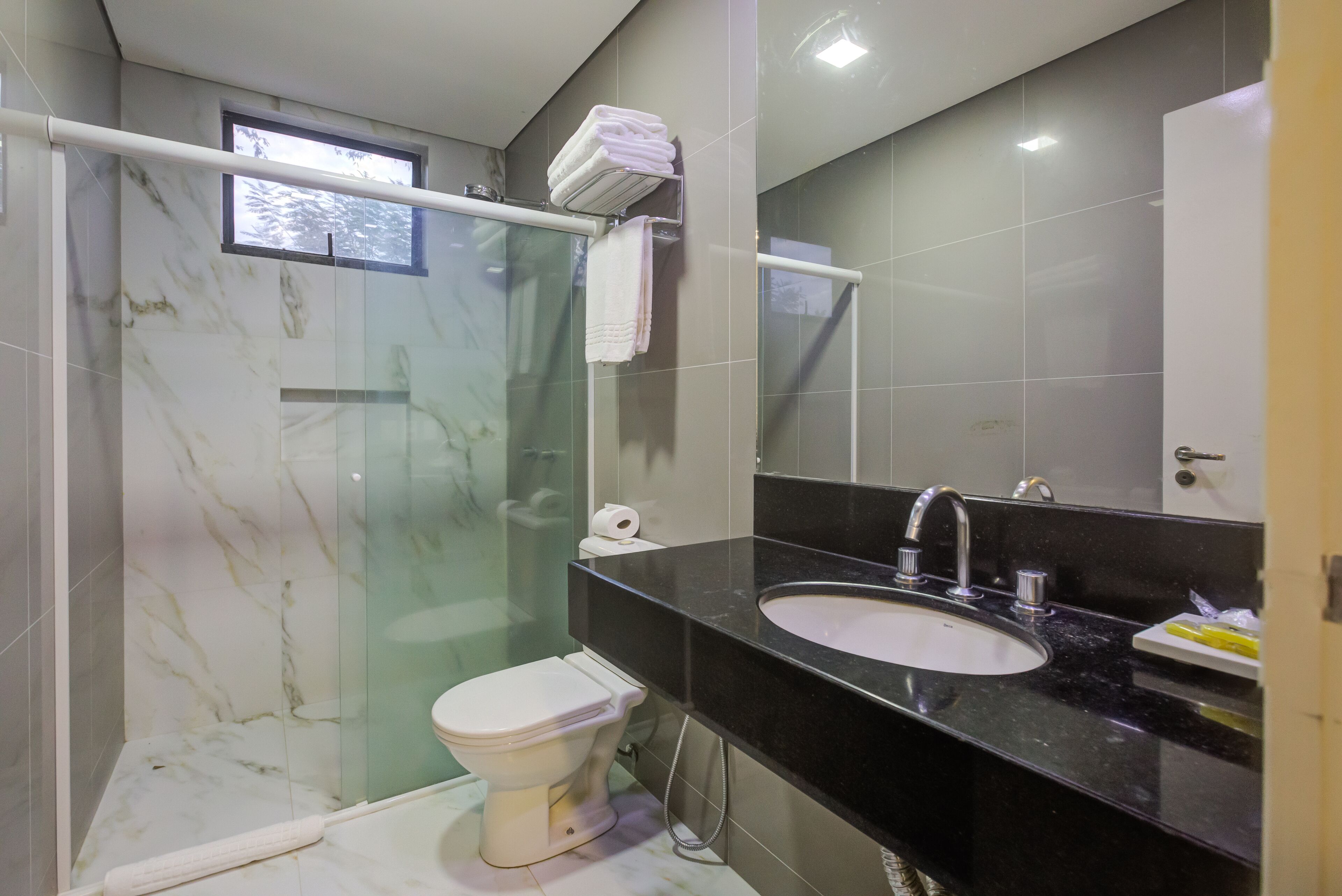 A modern bathroom with a glass-enclosed shower, a white toilet, a black countertop sink, and a mirror above the sink.