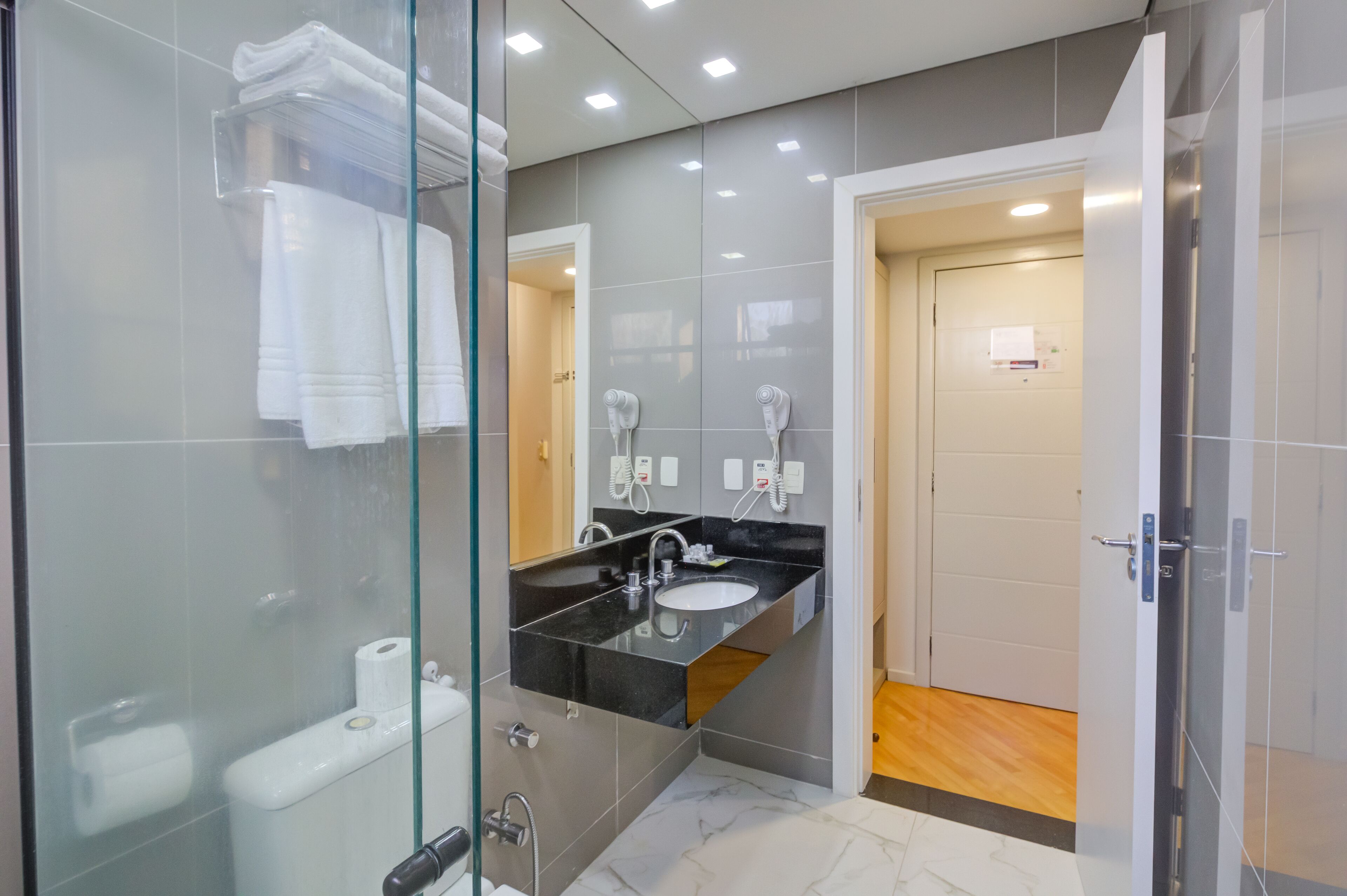 Un baño moderno con cabina de ducha de vidrio, lavamanos con encimera negra y rollo de papel higiénico a la vista.