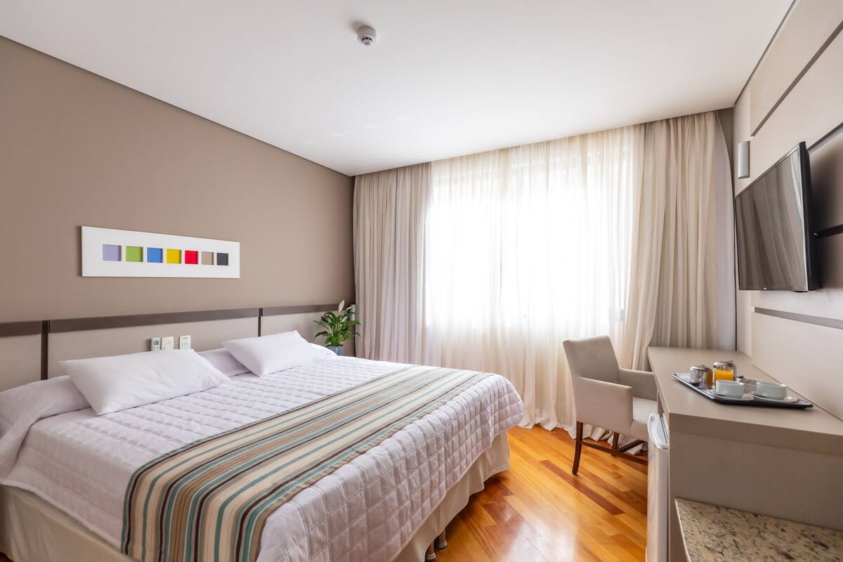 A hotel room with a bed, a desk, a television, and a window with curtains.