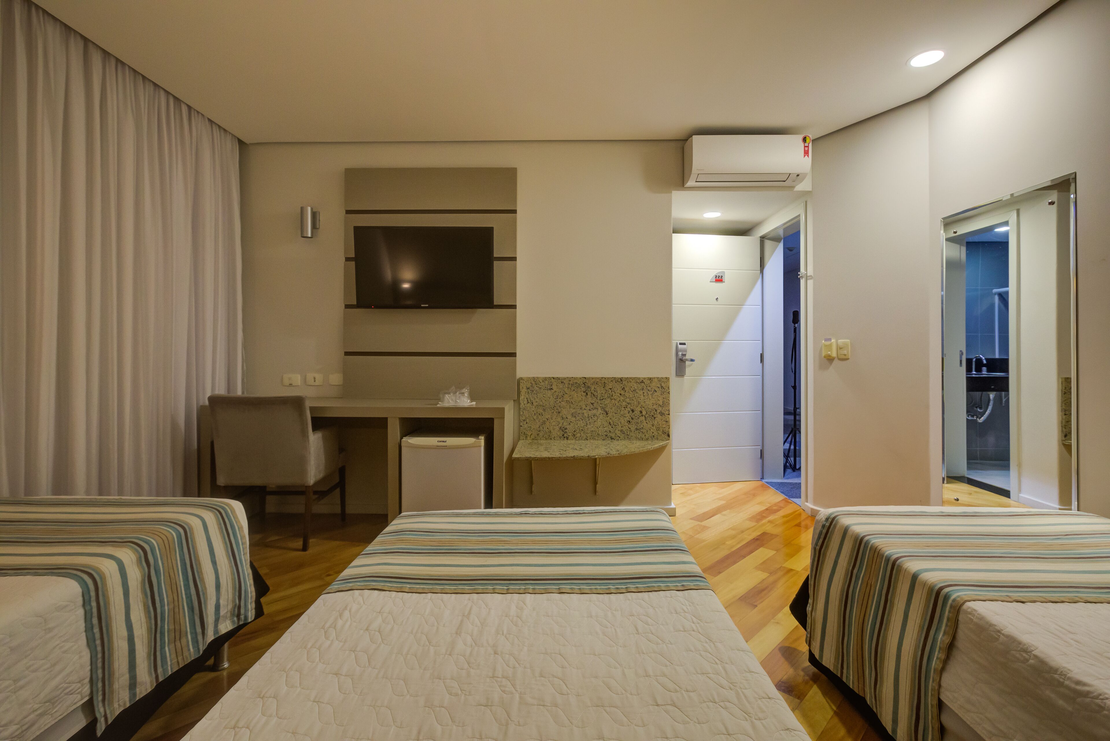 Habitación de hotel con dos camas, un escritorio, televisor y zona de ducha.