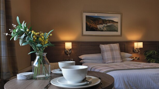 A hotel room with a bed, bedside tables, a dining table with bowls and a vase of flowers, and a framed picture on the wall. - Bannview Bed & Breakfast (Craigavon)