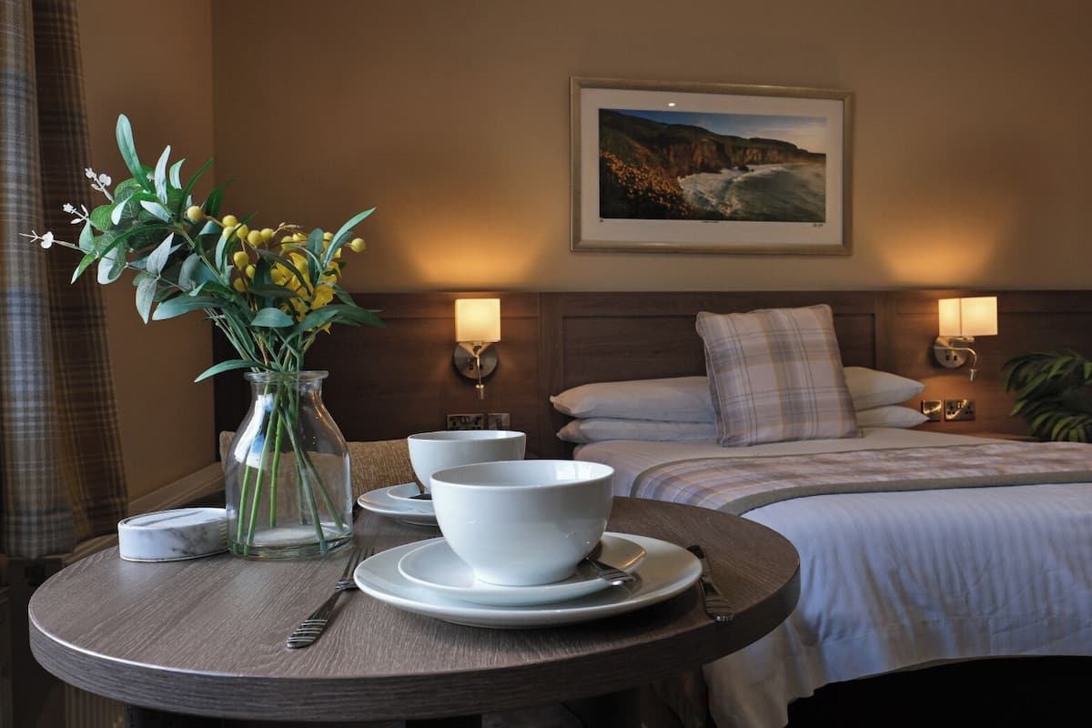 A hotel room with a bed, bedside tables, a dining table with bowls and a vase of flowers, and a framed picture on the wall.