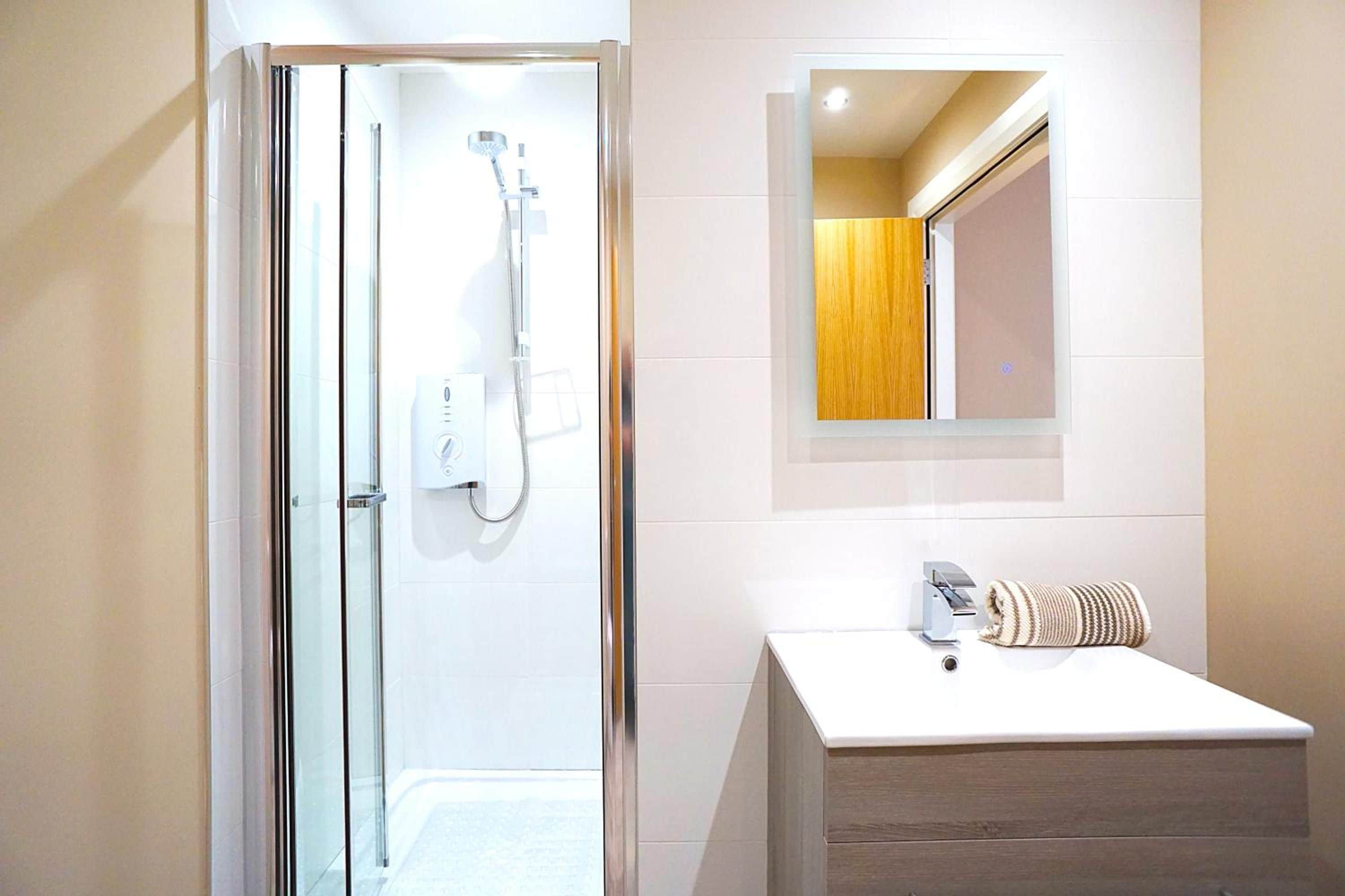A modern bathroom with a glass-enclosed shower, a white sink, and a wooden vanity.