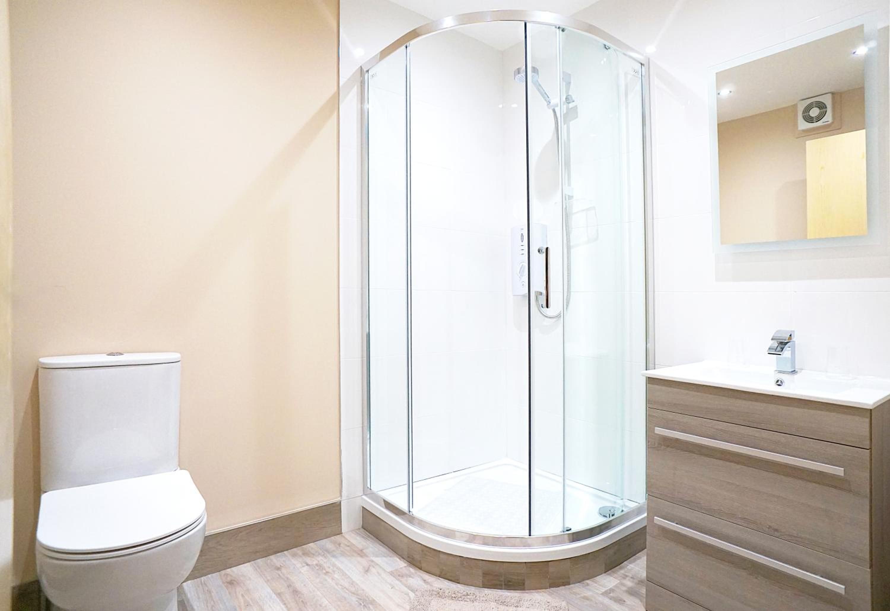 A modern bathroom with a glass-enclosed shower, a white toilet, and a wooden vanity with a mirror.