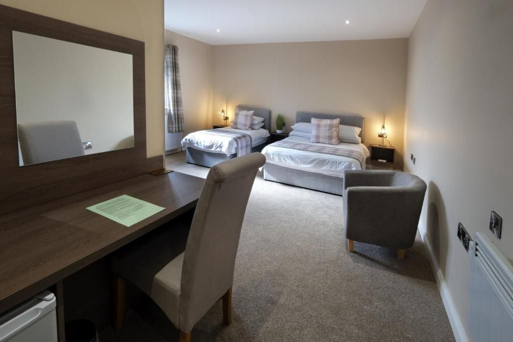 A hotel room with a desk, two beds, a chair, and a mirror.