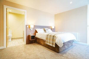 A bedroom with a bed, bedside lamps, a nightstand, a radiator, and a door leading to a bathroom.