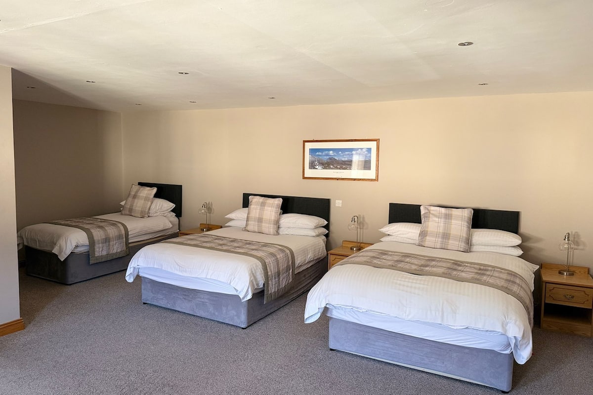 A hotel room with three single beds, each with a headboard, bedside tables, and a framed picture on the wall.