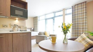 A modern kitchen with a microwave, coffee maker, and kettle. There is a round table with a yellow mug and a vase of flowers. A sofa and a chair are in the living area with a large window and curtains. - Bannview Bed & Breakfast (Craigavon)