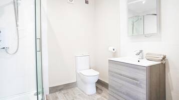 Une salle de bain moderne avec une douche à parois de verre, des toilettes blanches et un meuble-lavabo avec un miroir.