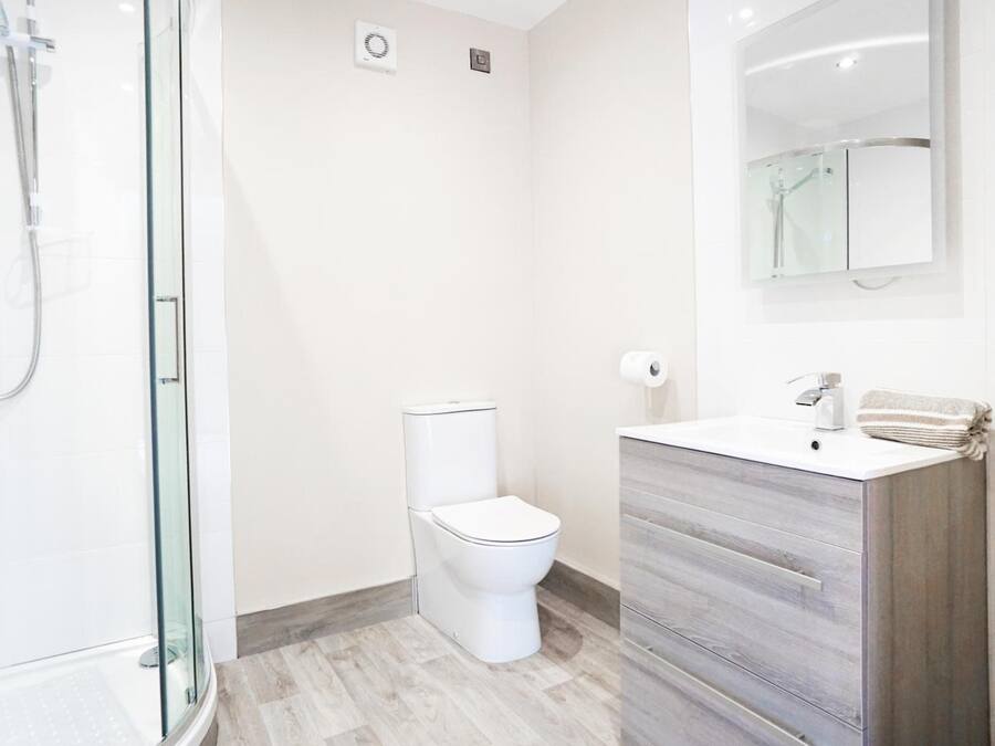 Une salle de bain moderne avec une douche à parois de verre, des toilettes blanches et un meuble-lavabo avec un miroir.