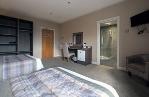 Habitación de hotel con dos camas, un escritorio, una silla, un refrigerador pequeño, un televisor y zona de ducha.