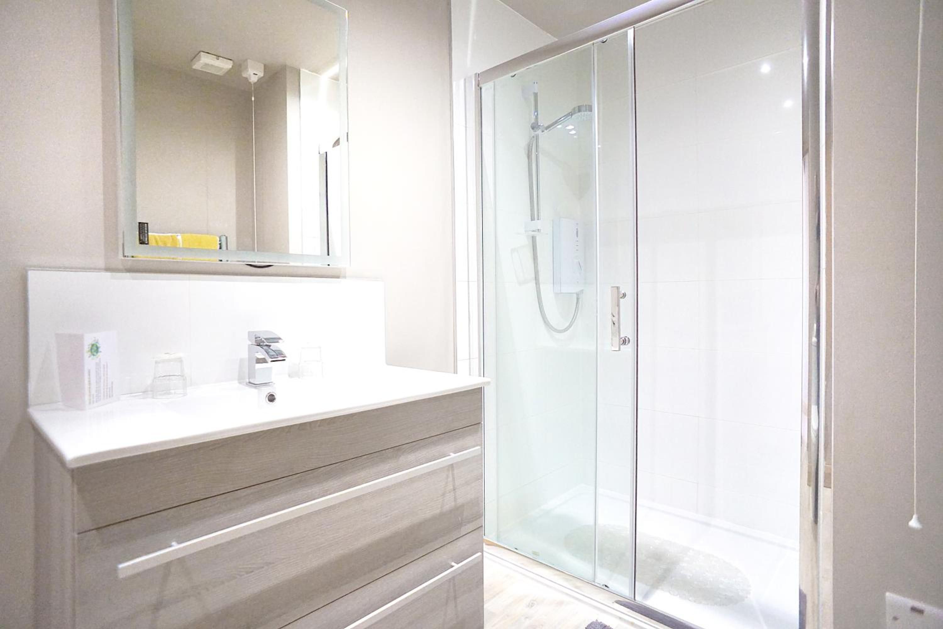 A modern bathroom with a glass-enclosed shower, a white vanity with a mirror, and a light-colored floor.