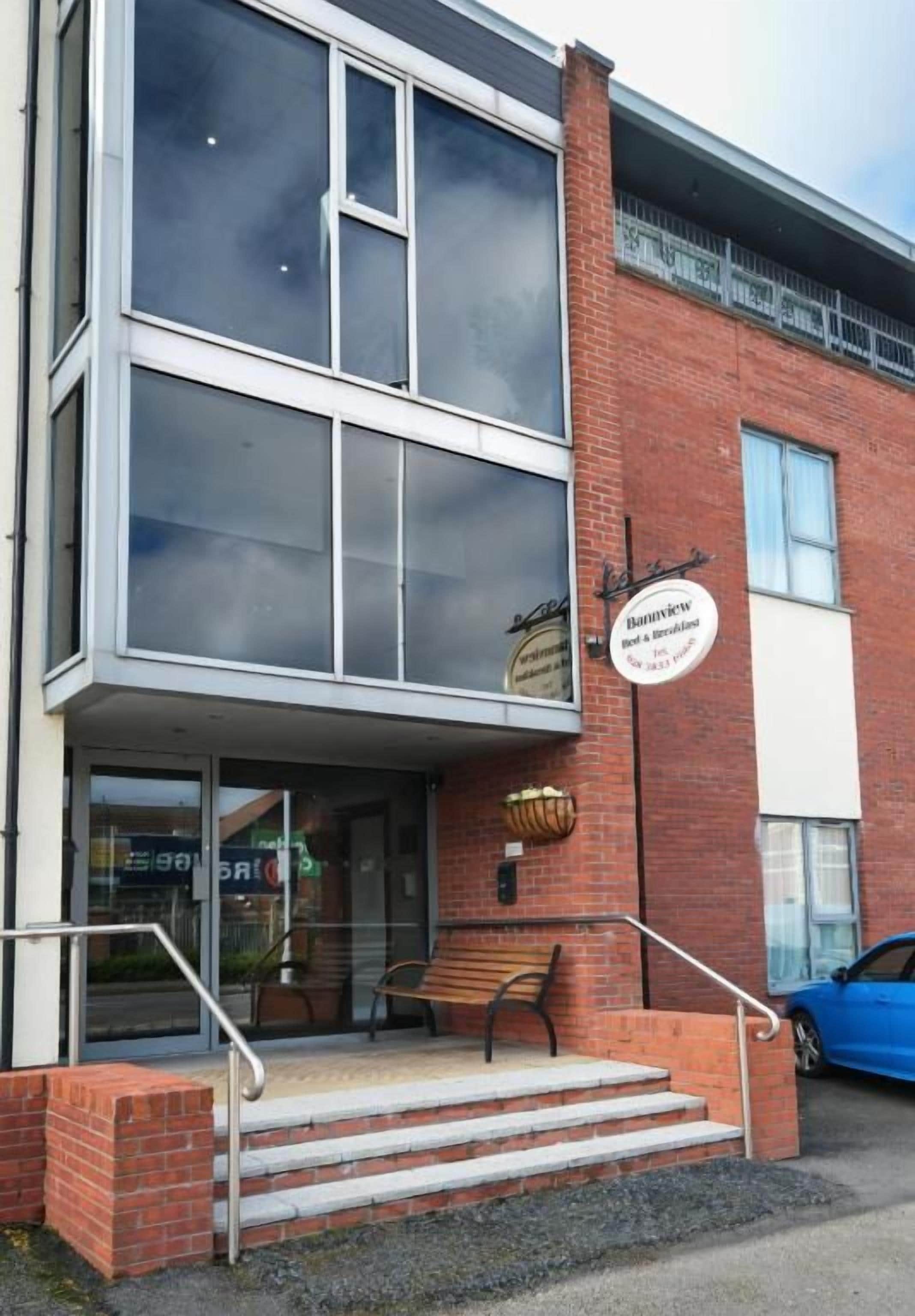 A two-story building with a brick facade, a glass entrance, and a bench outside.
