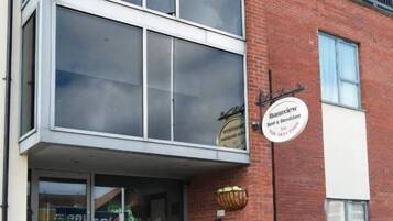 A two-story building with a brick facade, a glass entrance, and a bench outside.