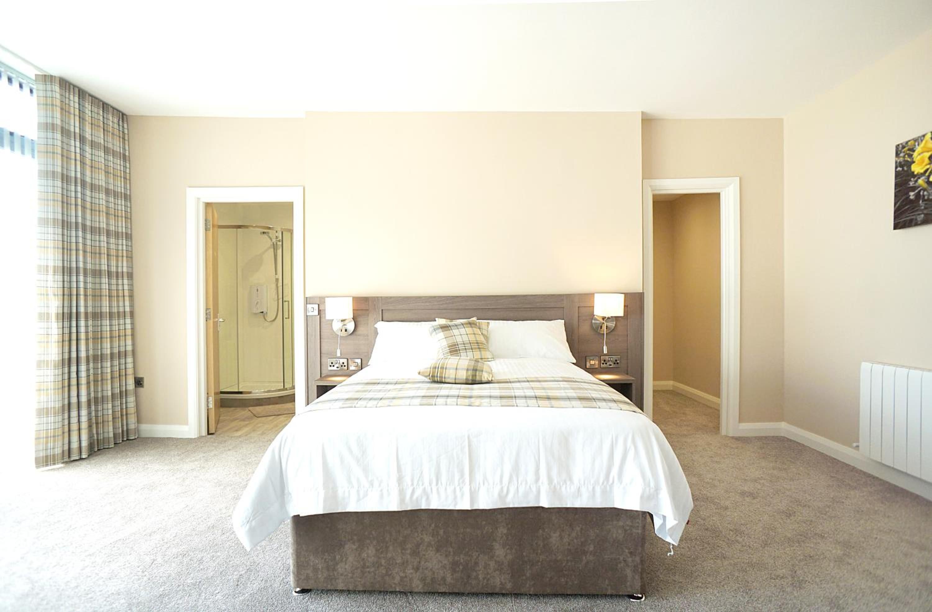 A hotel room with a bed, bedside lamps, a radiator, and a door leading to a bathroom.