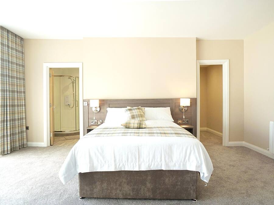 A hotel room with a bed, bedside lamps, a radiator, and a door leading to a bathroom.